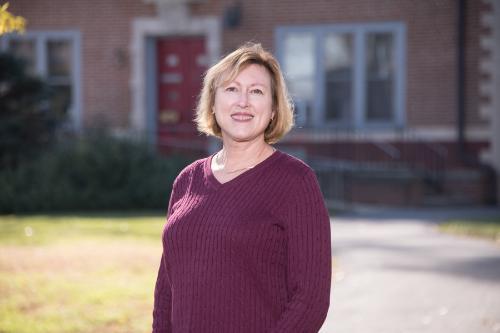 Woman in auburn hued long-sleeve shirt standing in front of Gabriel House on Muhlenberg College campus.